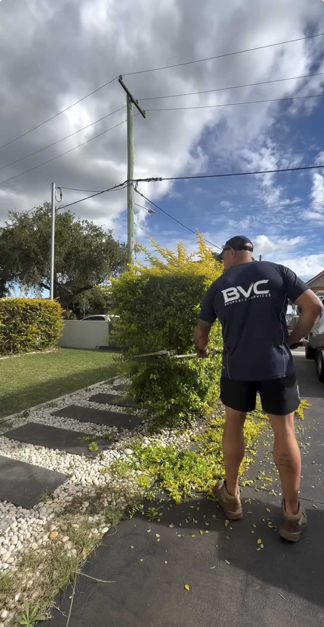 BVC crew member in a navy BVC shirt trimming a hedge